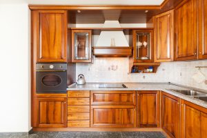 Eine moderne Küche mit Holzschränken, eingebautem Ofen, Edelstahlspüle und gefliester Küchenrückwand, bereit für die Wohnungsräumung.
